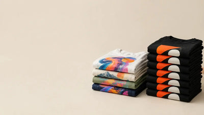 Folded t-shirts with colorful full-color prints beside a stack of simple two-color prints, illustrating dtf vs screen printing